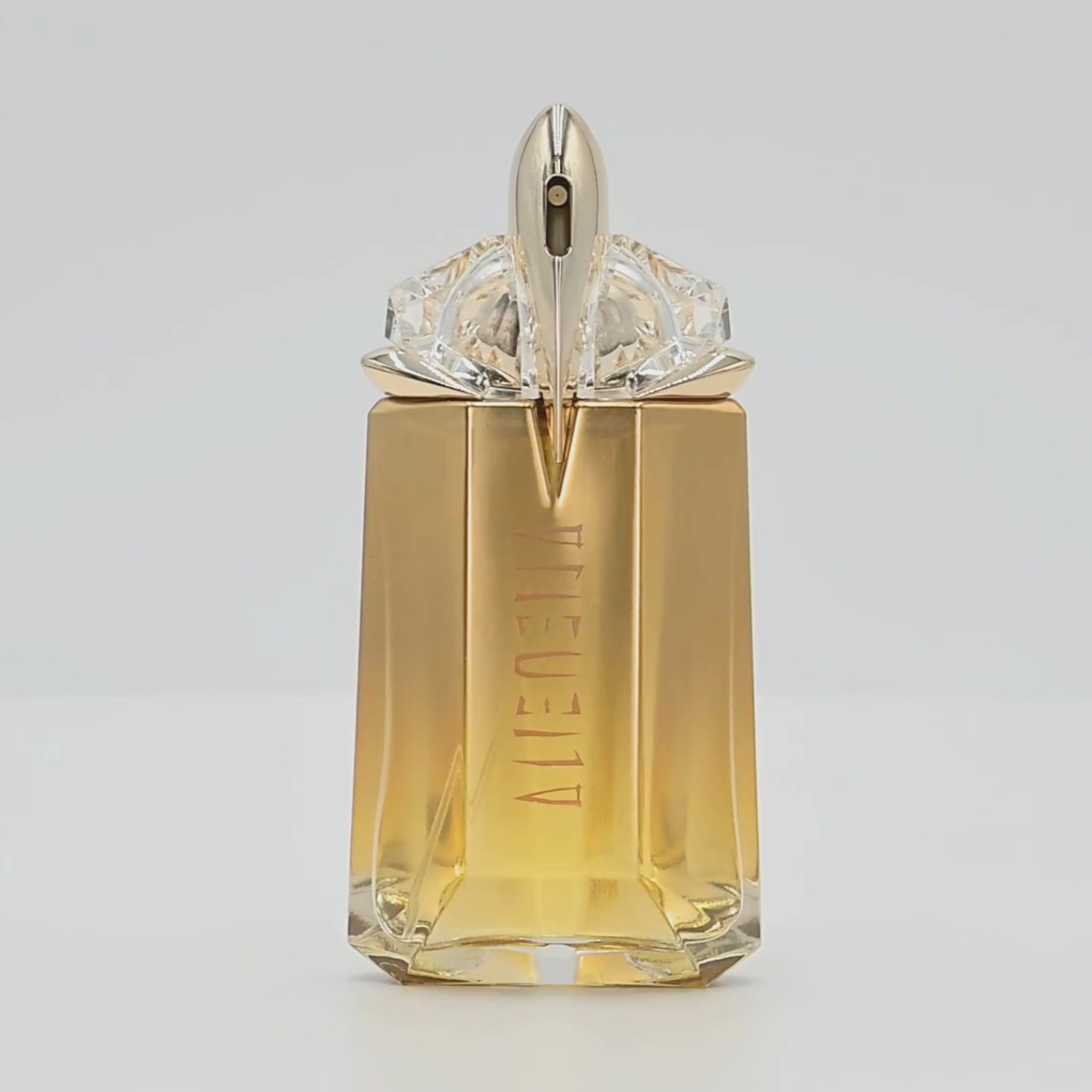 Mugler Alien perfume bottle rotating on a white podium
