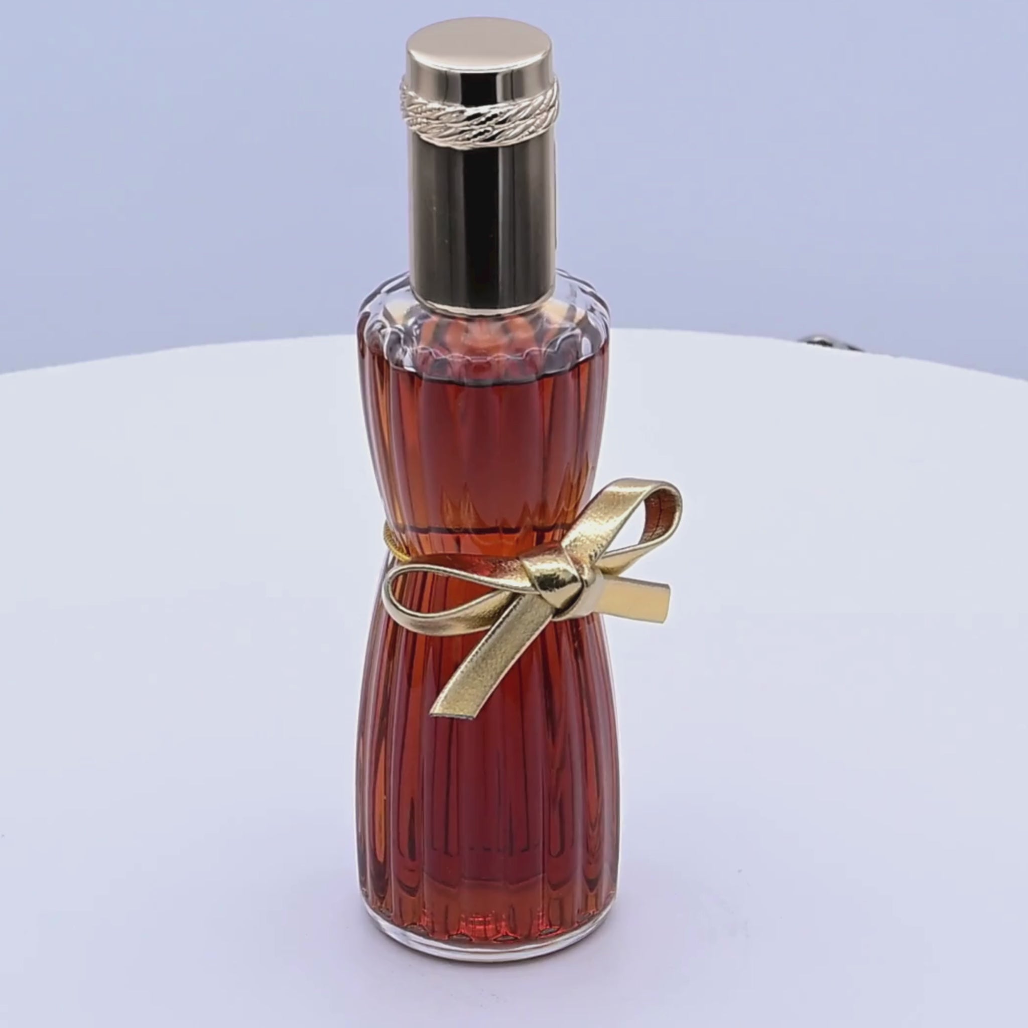 Brown perfume bottle with gold cap and ribbon rotating on a white podium