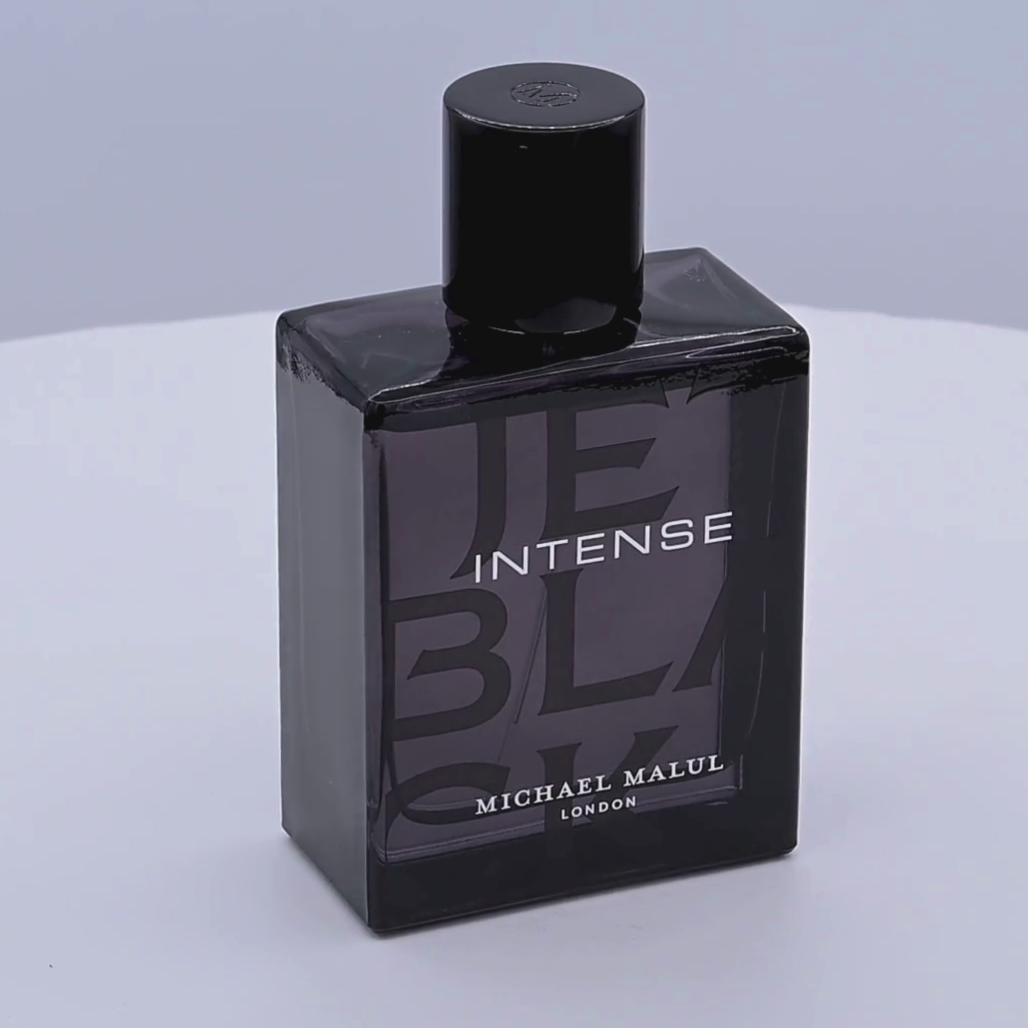Black perfume bottle labeled 'Intense' by Michael Malul rotating on a white podium