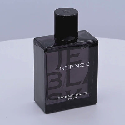 Black perfume bottle labeled 'Intense' by Michael Malul rotating on a white podium