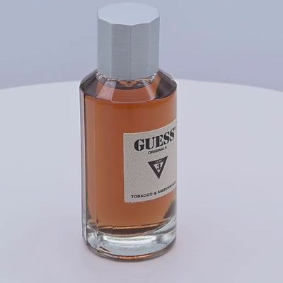 Guess Tobacco & Amberwood perfume bottle rotating on a white podium