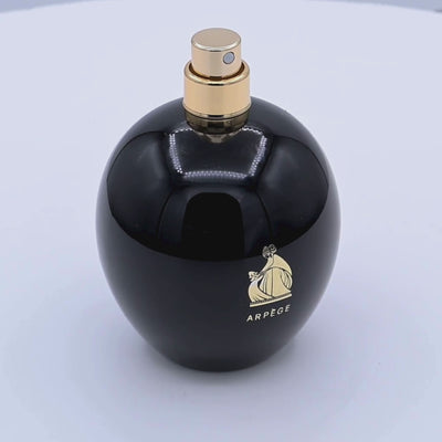 Black perfume bottle with gold cap and Arpege logo rotating on a white podium