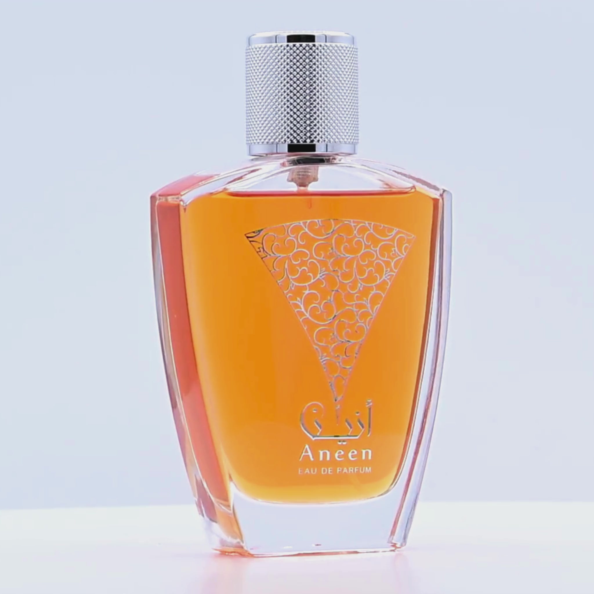 Orange Aneen perfume bottle with silver cap rotating on a white podium