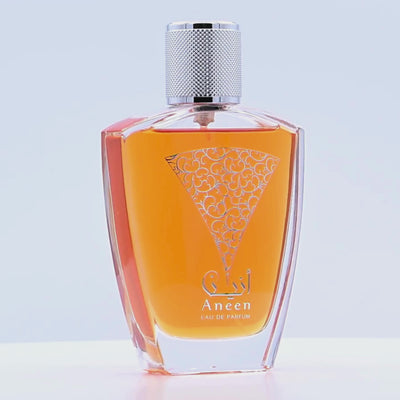 Orange Aneen perfume bottle with silver cap rotating on a white podium