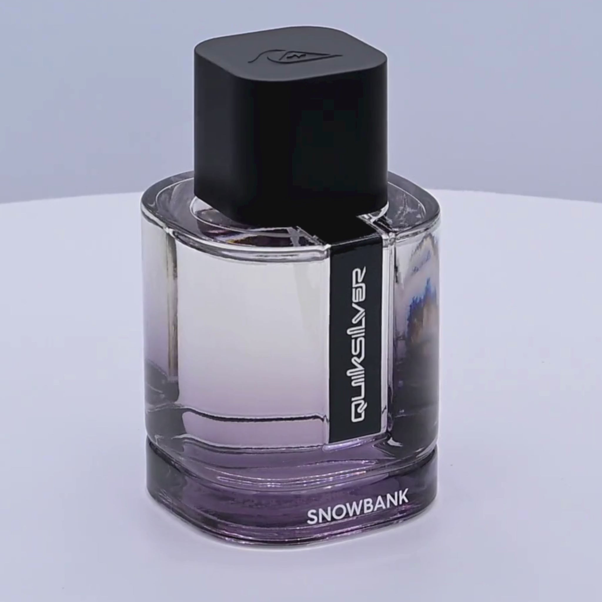 Clear perfume bottle with black cap and 'Quiksilver Snowbank' label rotating on a white podium