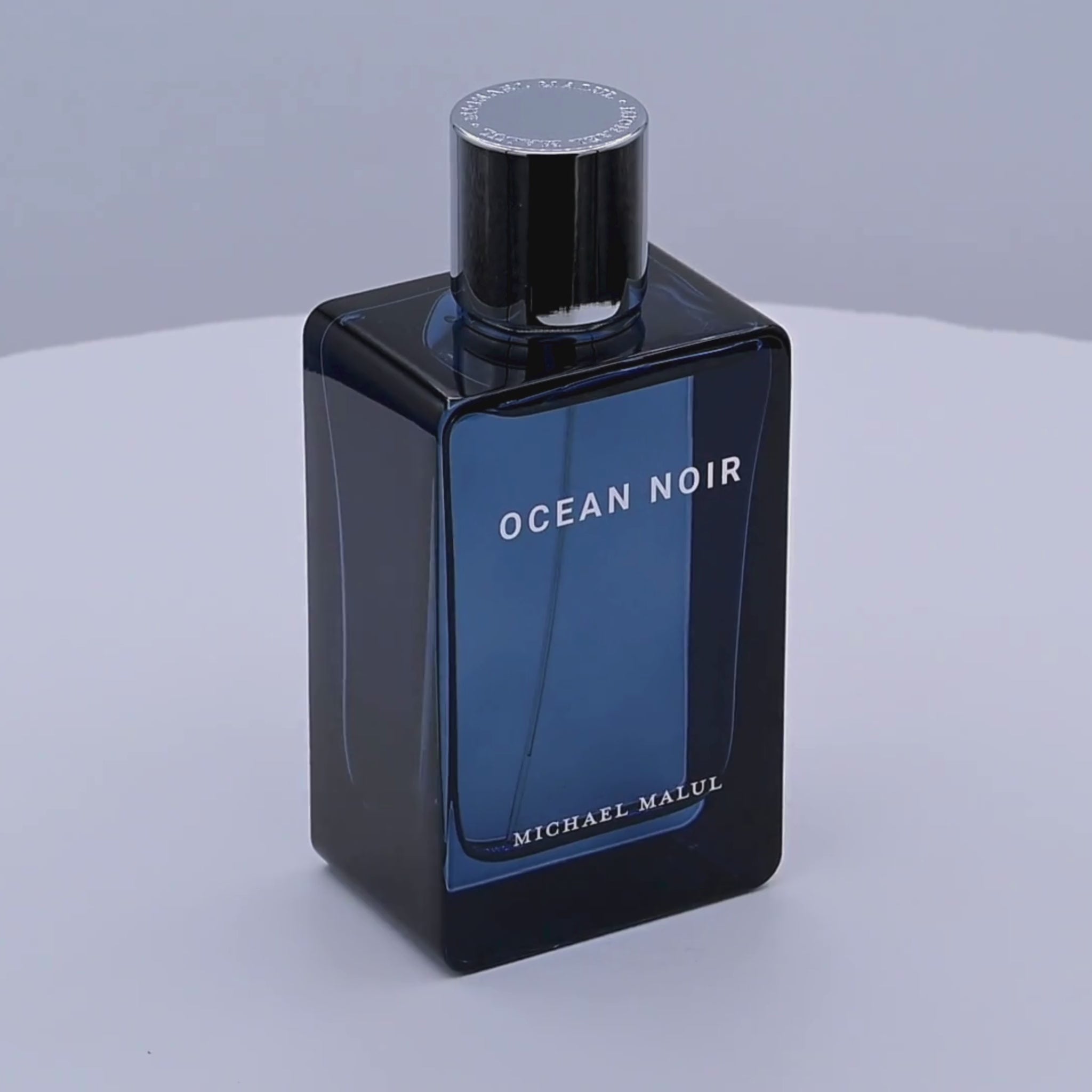 Perfume bottle of 'Ocean Noir' by Michael Malul rotating on a white podium