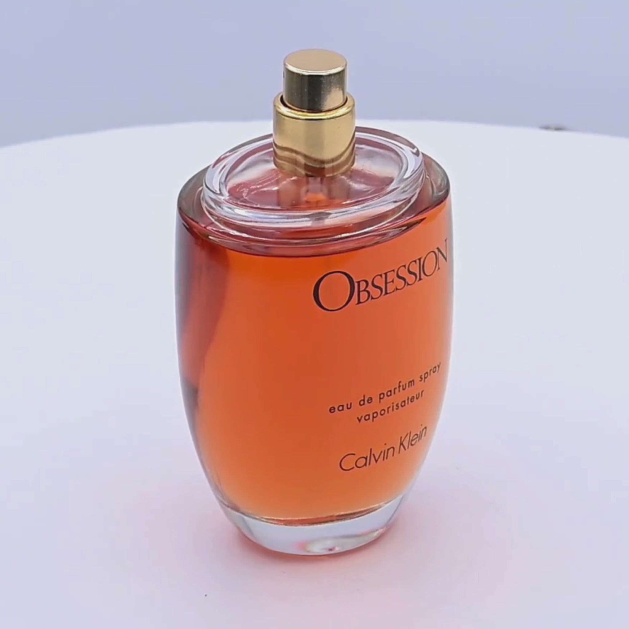 Calvin Klein Obsession perfume bottle rotating on a white podium